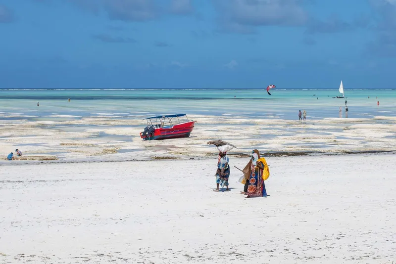 Low-tide beach with a red boat, kites in the sky and two women walking on the sand