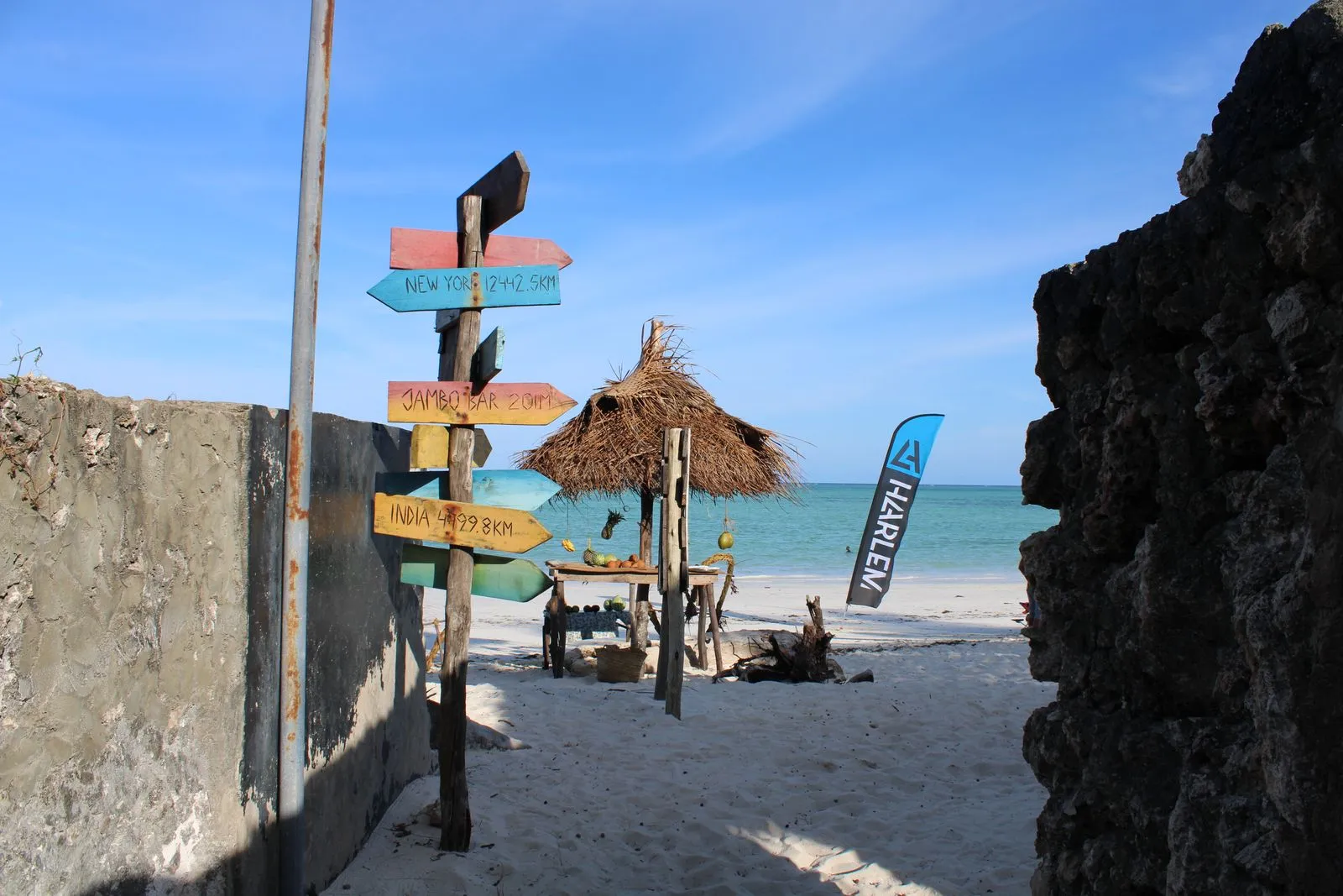Wooden direction signpost on Paje beach with a thatched sunshade and the sea behind