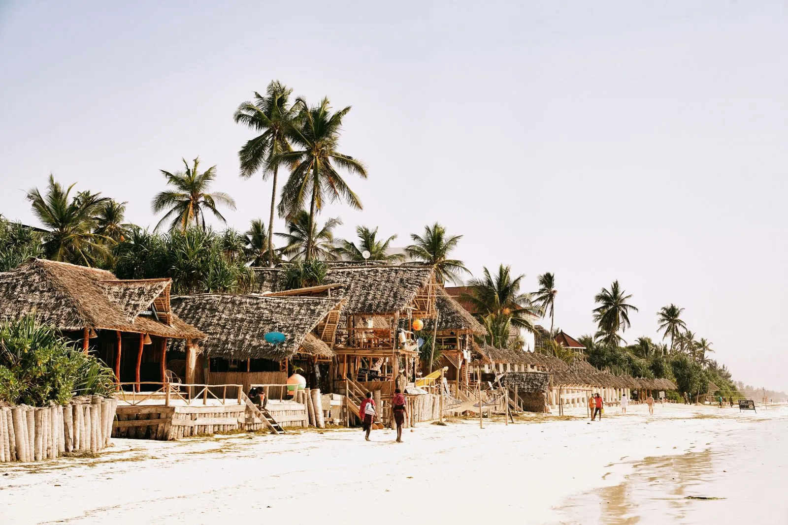 Thatched beach bars and huts under palm trees along a white-sand beach