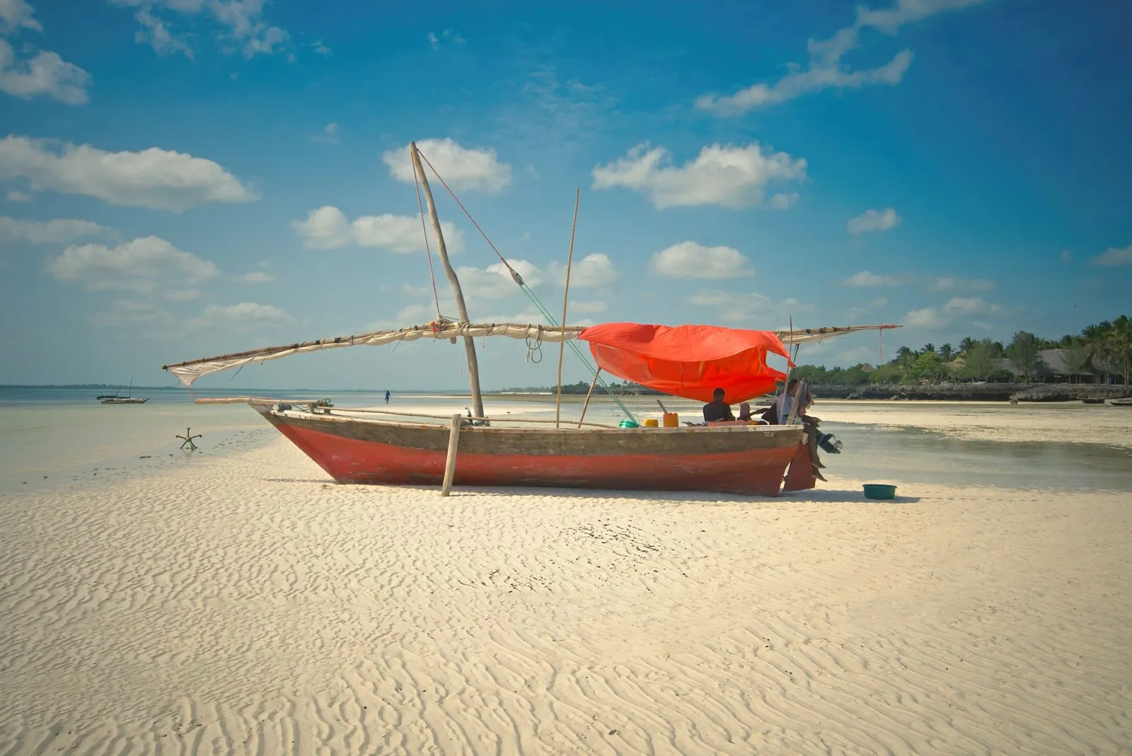 Wooden dhow with a red sail cover on a sandy beach at low tide