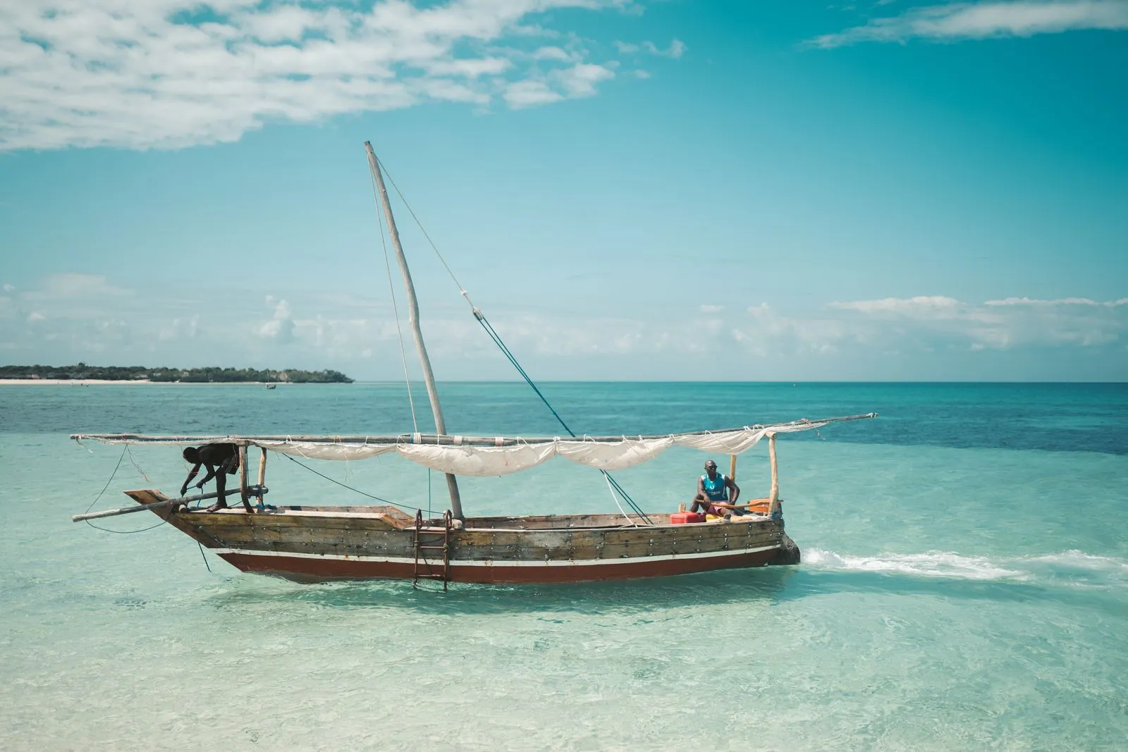 Wooden dhow with two fishermen in clear turquoise water off the Zanzibar coast