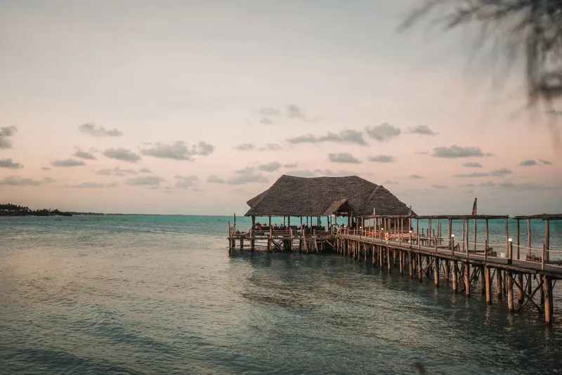 Wooden jetty with a thatched pavilion over calm water at sunset