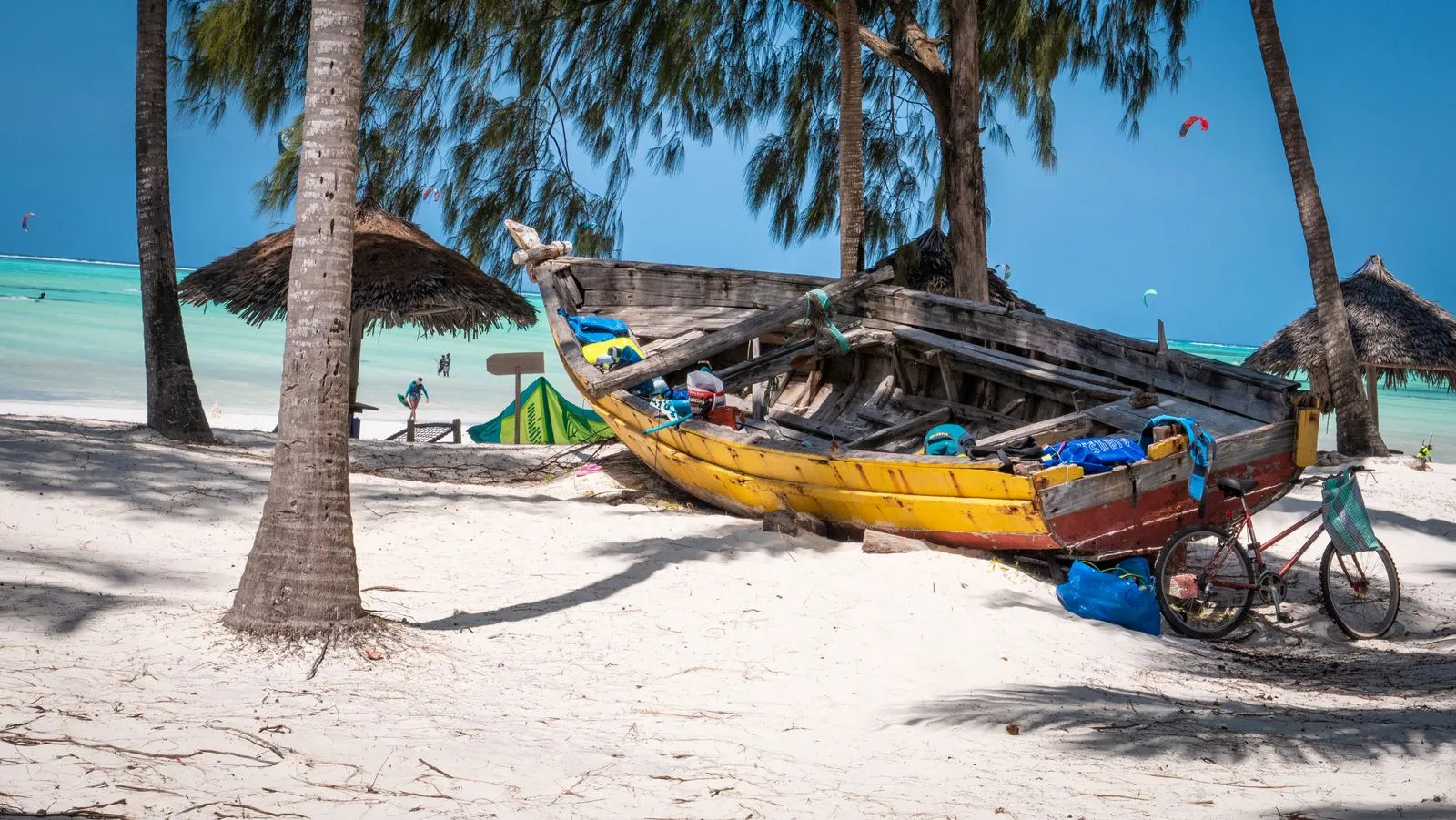 Old wooden boat and a bicycle under palm and casuarina trees on a white-sand beach