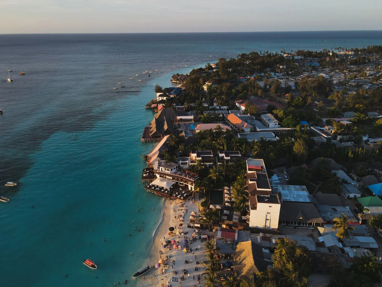 Aerial view of beach hotels and a village along turquoise water on the Zanzibar coast