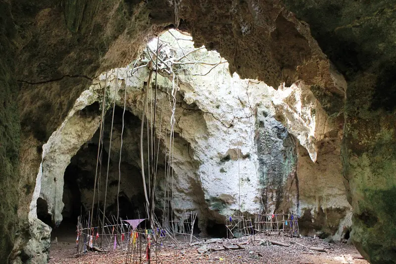 Main chamber of Kuumbi Cave lit through a hole in the roof, with stick fences and cloth offerings