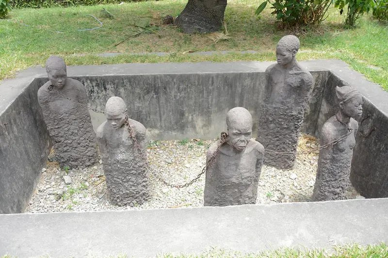 Stone figures in chains standing in a pit at the slave market memorial in Stone Town