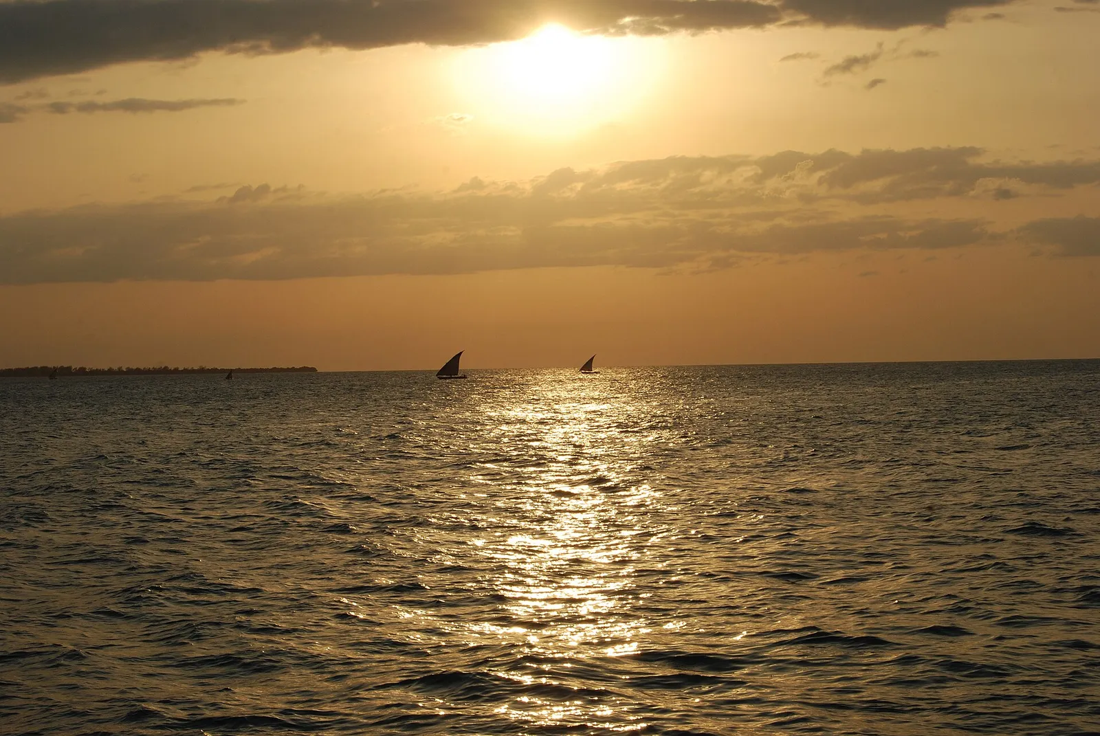 Sun setting over the sea off Stone Town with two dhows on the horizon