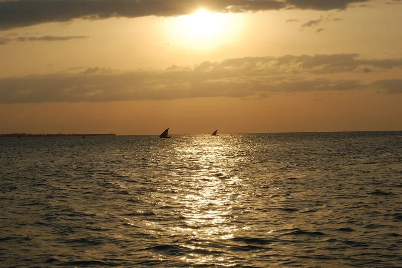 Sun setting over the sea off Stone Town with two dhows on the horizon