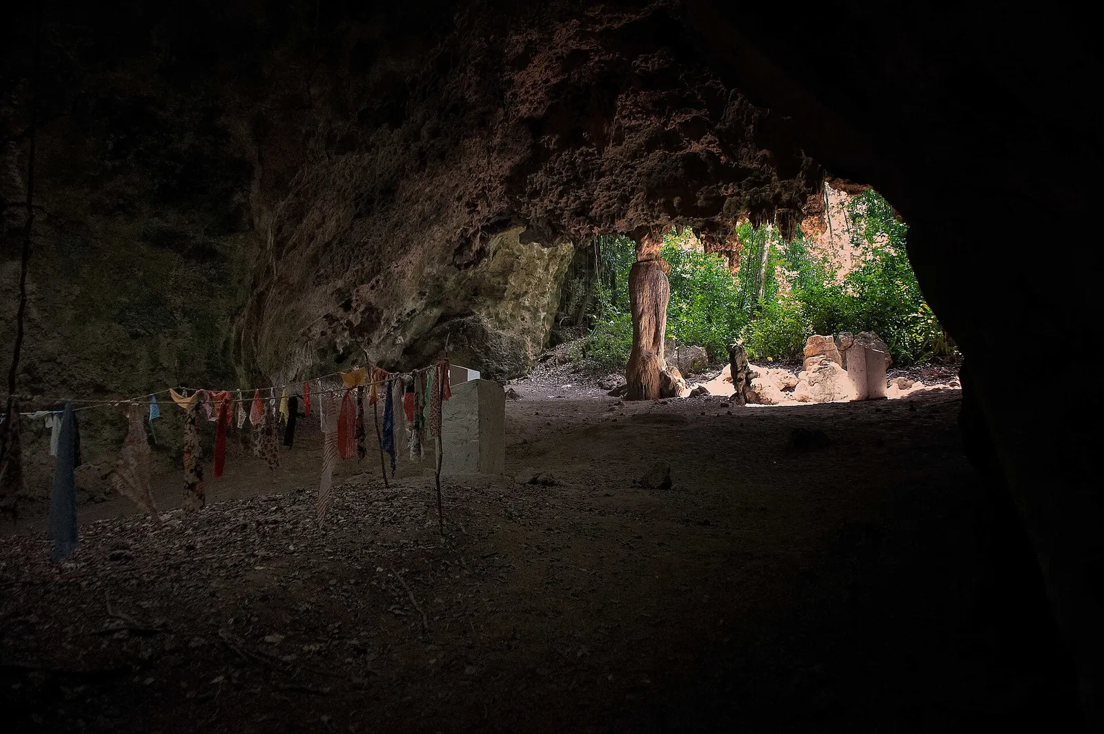 Inside Kuumbi Cave, with offering cloths on a line and daylight at the entrance