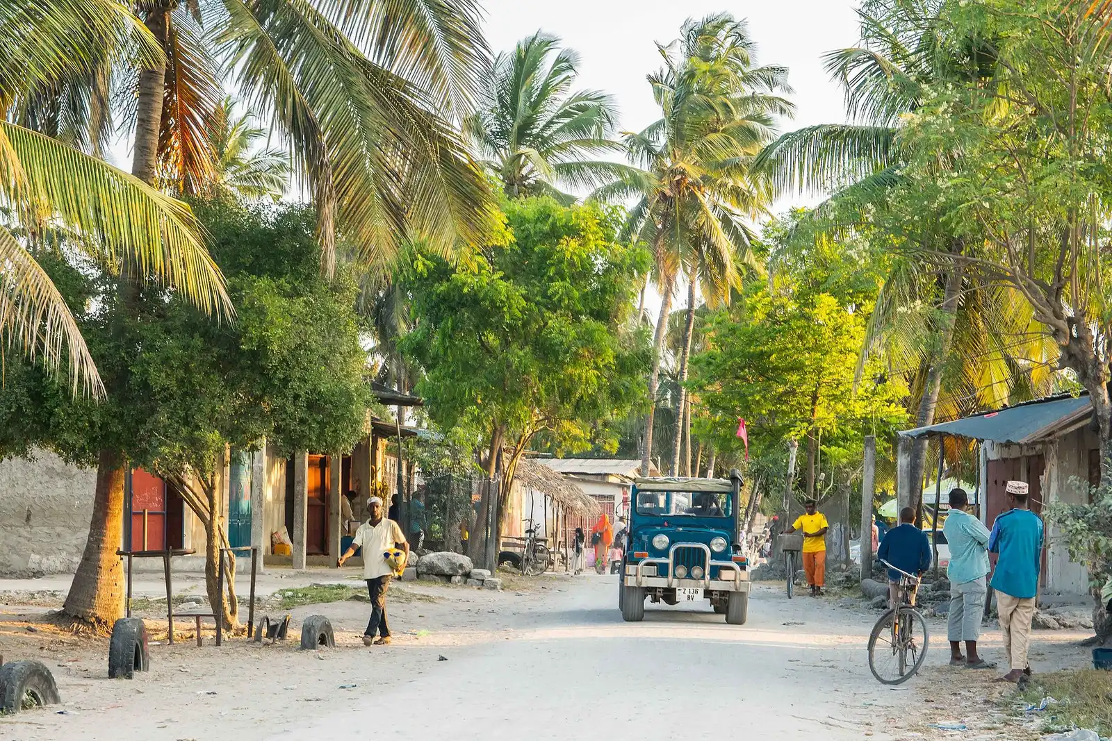 Sandy village road under coconut palms in northern Zanzibar with a jeep and people walking