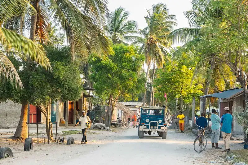 Sandy village road under coconut palms in northern Zanzibar with a jeep and people walking