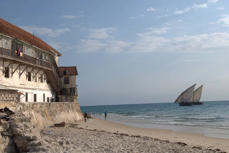 Two dhows under sail off the beach below an old Stone Town seafront building