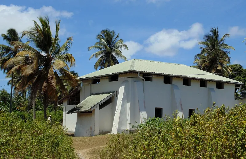 Kizimkazi mosque from outside: a whitewashed building with a green tin roof among palms