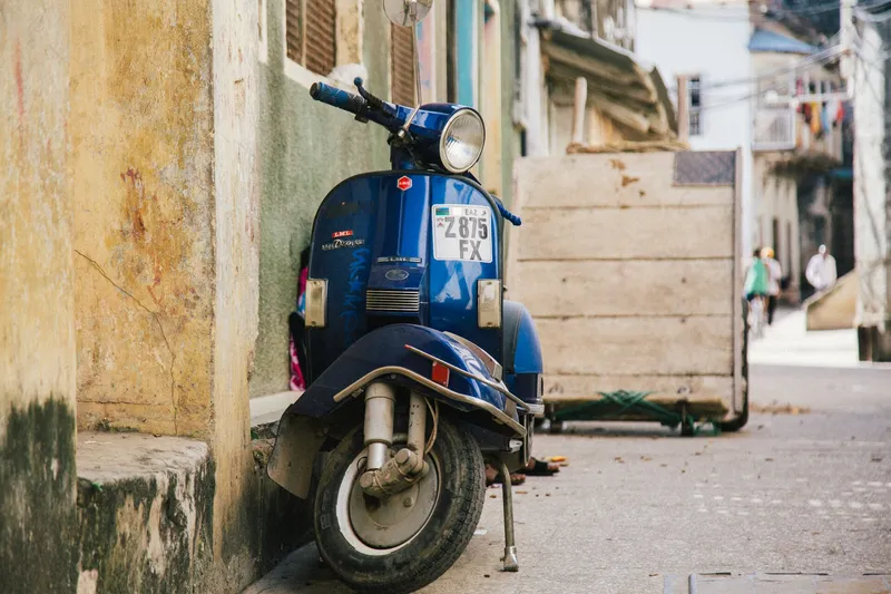 Blue Vespa scooter parked against a weathered wall in a Stone Town lane